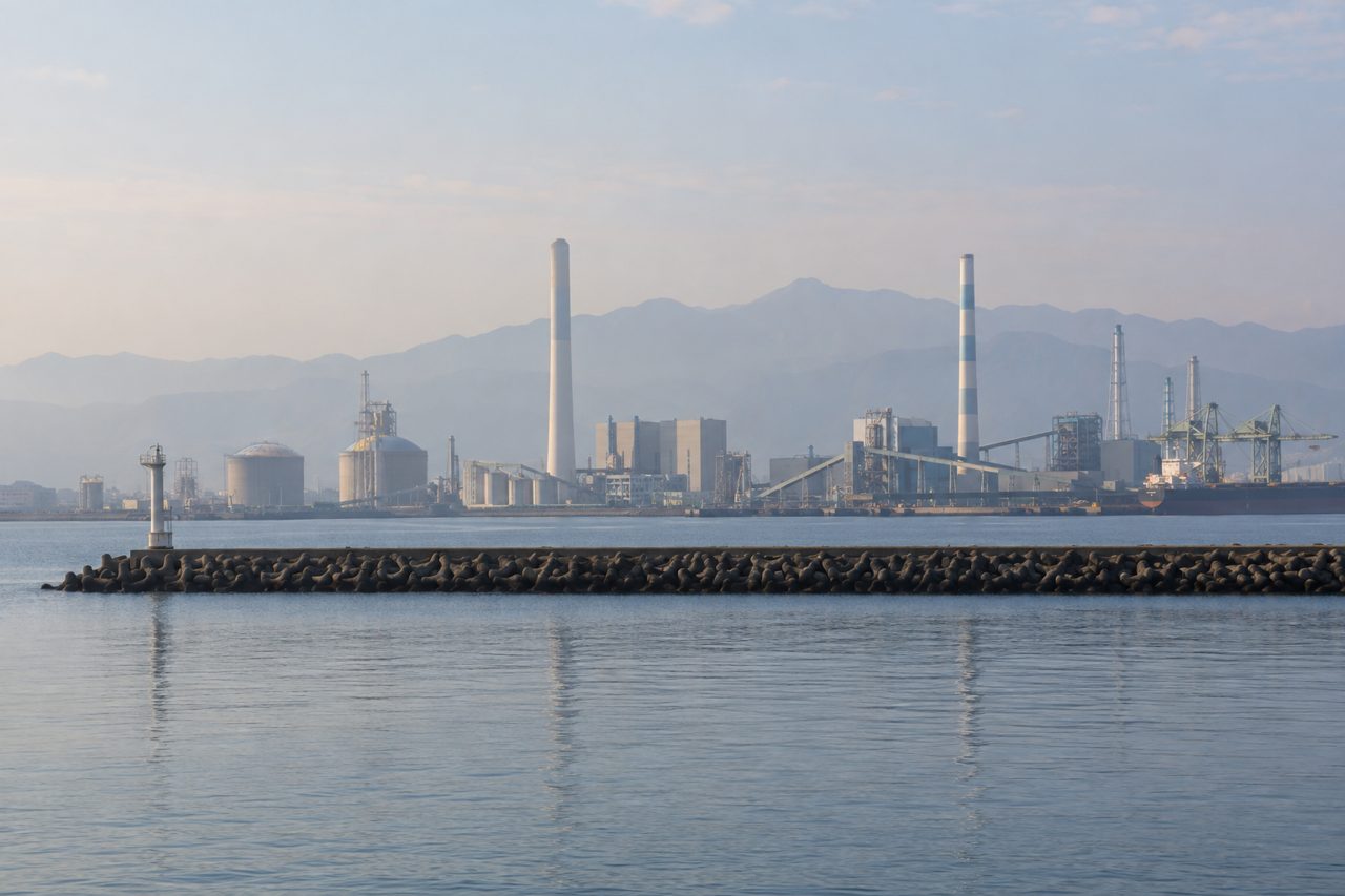 工業港の発電設備を遠景に望む静かな海辺