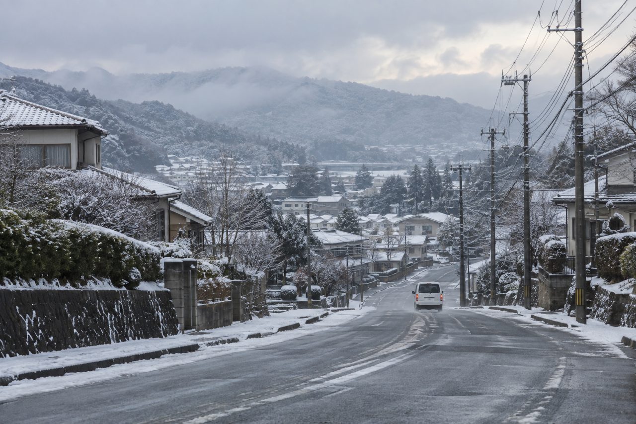 雪の住宅街をゆっくり進む無地の配送車の遠景