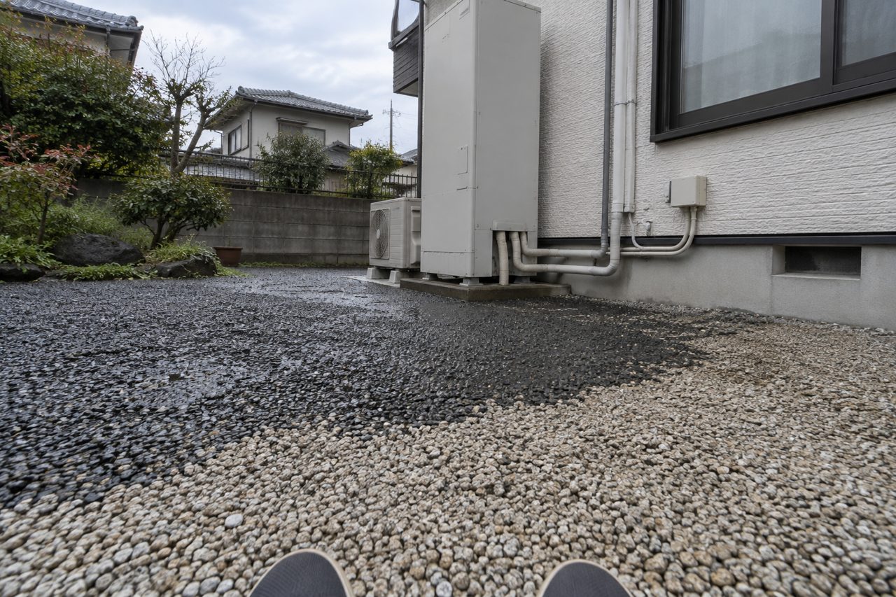 濡れた砂利の境目から貯湯タンクを見上げる足元