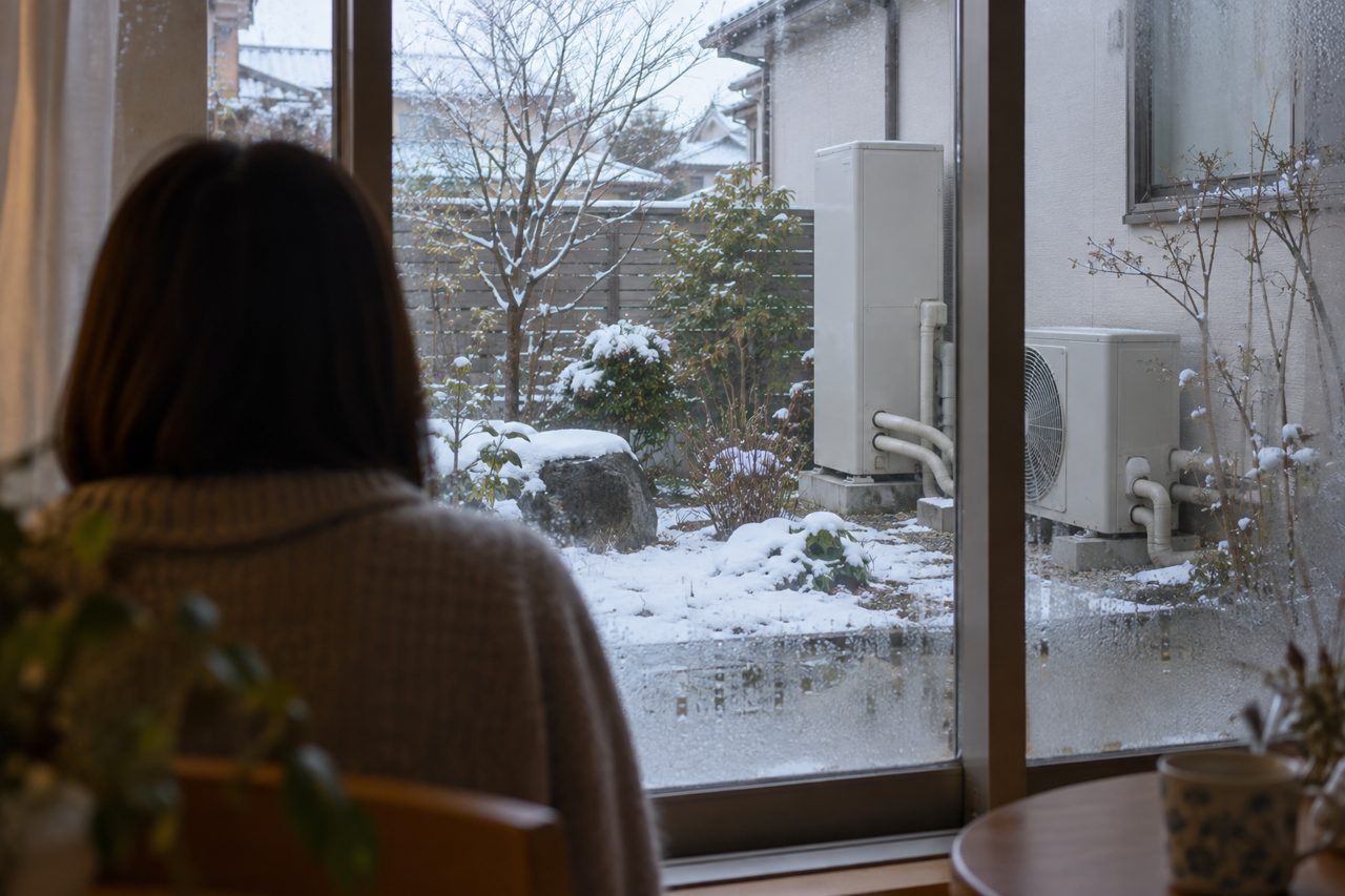 冬の窓越しに保温配管と室外機を確認する住人