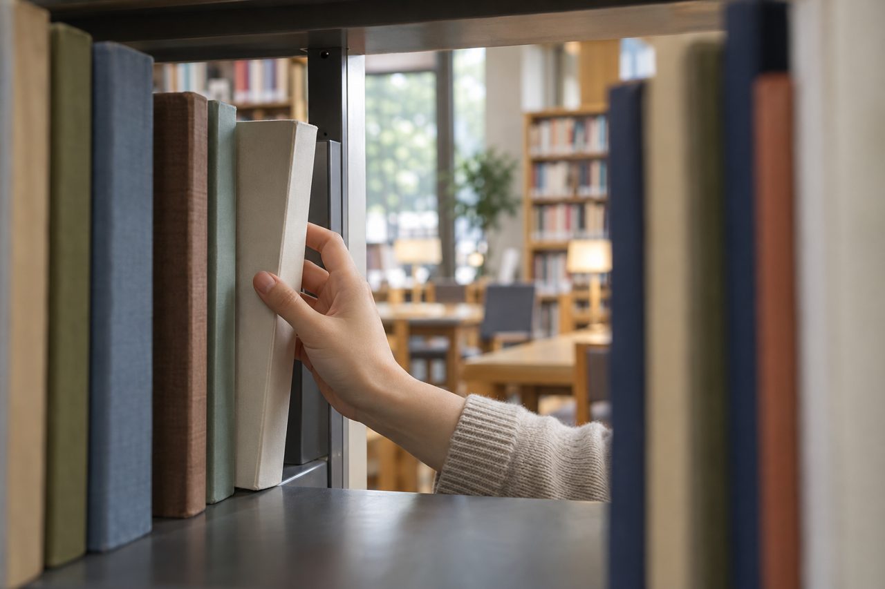 図書館の棚から語学教材を選ぶ学生の手元